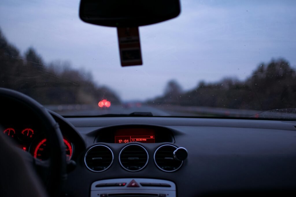 Car dashboard and windshield view on a highway at twilight with illuminated dials and road ahead.